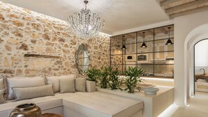 Una sala de estar moderna con una pared de piedra, un sofá grande, una mesa de centro de madera y una zona de cocina con armarios y un lavamanos.