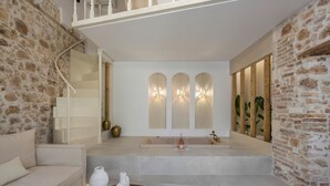 Un baño moderno con una bañera independiente, un tocador blanco y una pared de piedra.