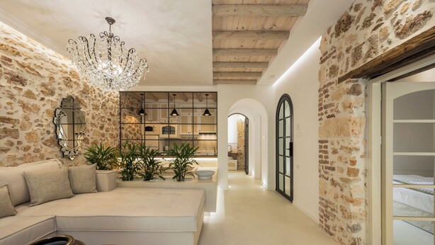 Un interior moderno con paredes de ladrillo a la vista, una zona de estar central con un sofá y una mesa de centro, y una cocina con iluminación colgante.