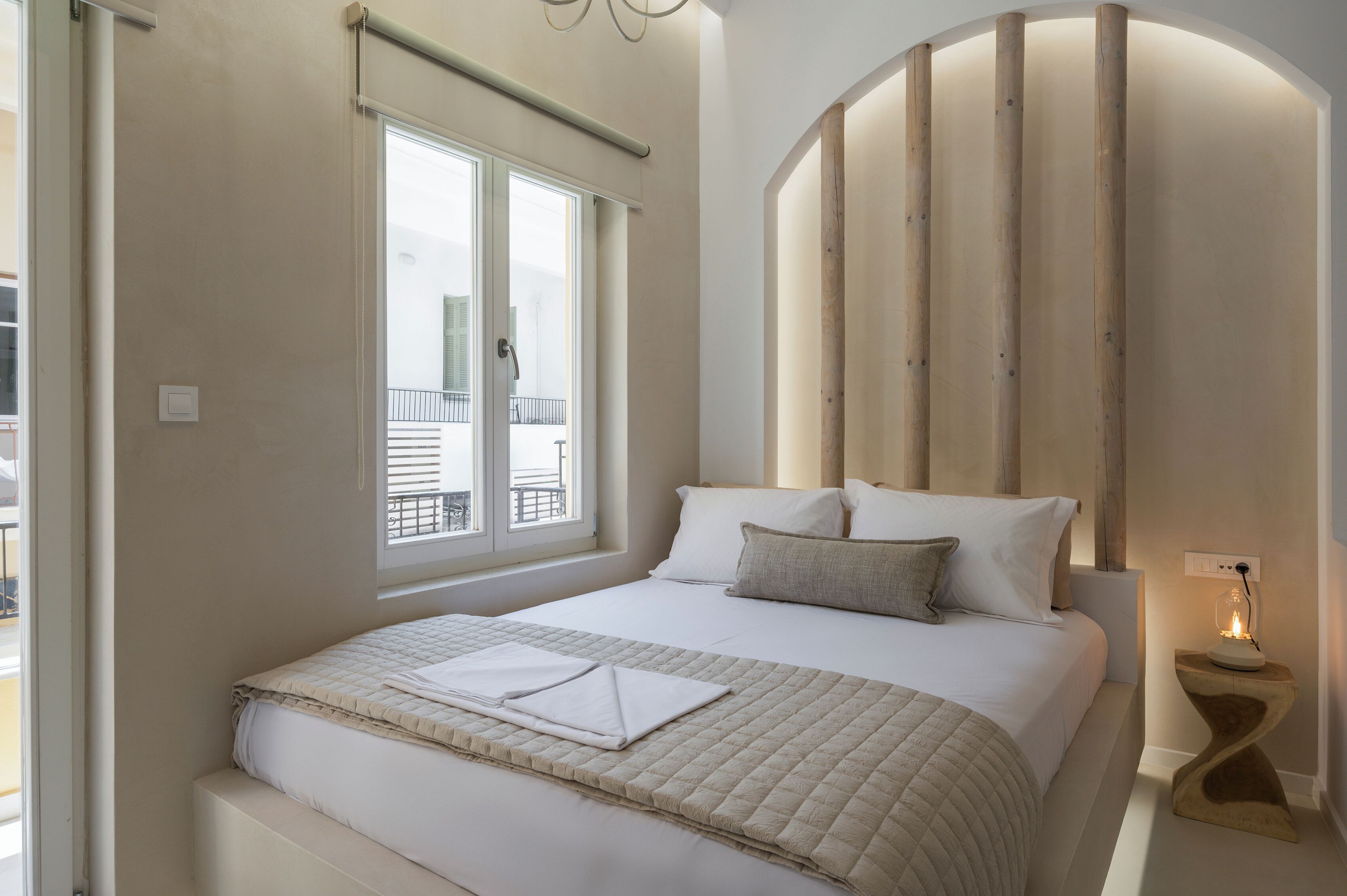 A bedroom with a large bed, a window, and a bedside table with a lamp.