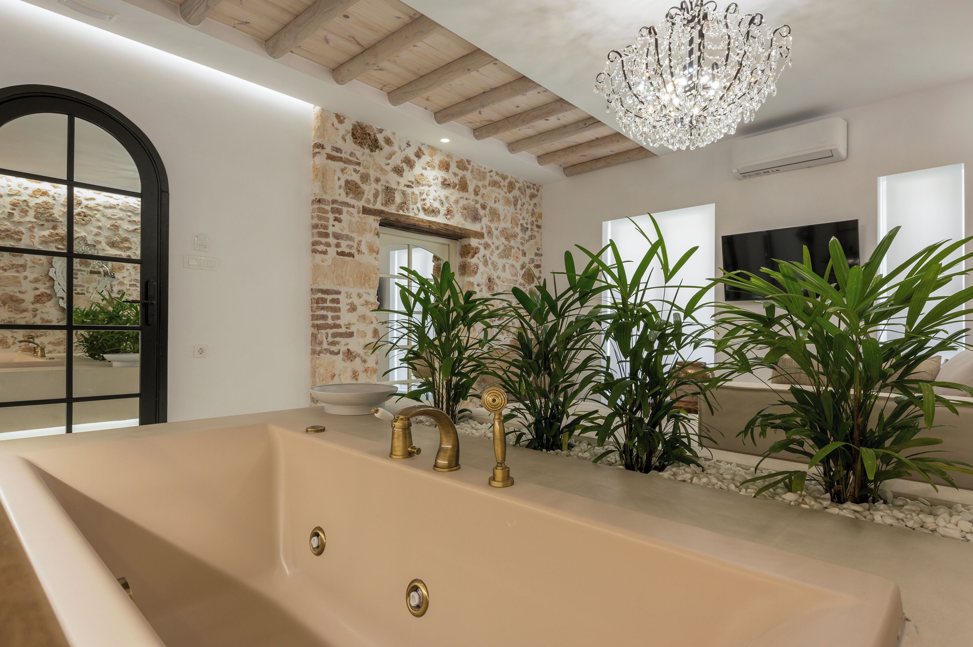 A bathroom with a large bathtub, a stone wall, and a chandelier.