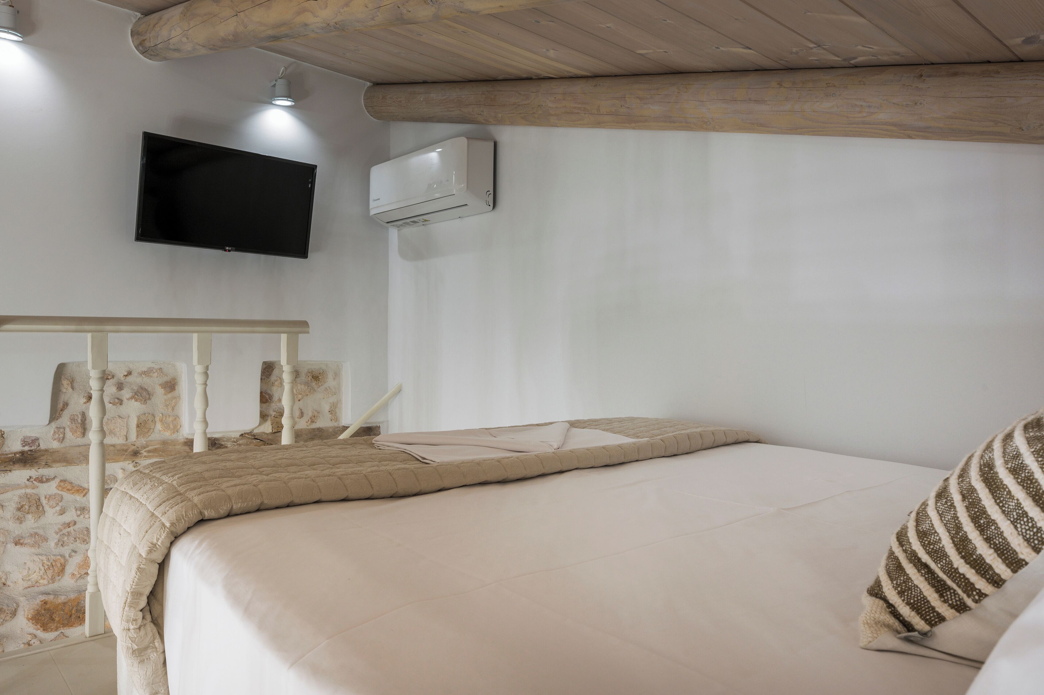 Un dormitorio con una cama, un televisor de pantalla plana montado en la pared y un equipo de aire acondicionado.