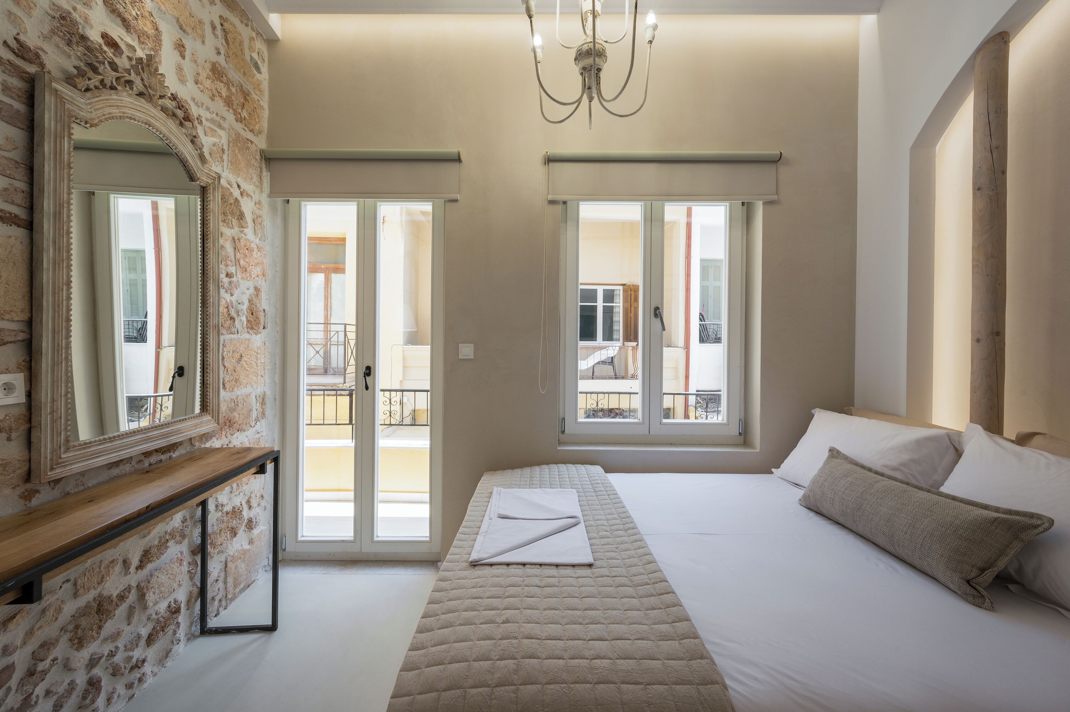 A bedroom with a large bed, a wooden bench, a mirror, and a view of the outside balcony.
