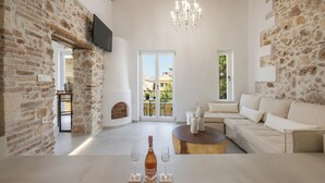 Amplia sala de estar con pared de piedra, techo de madera, sofá blanco, una mesita de centro y una botella de vino sobre una mesa.