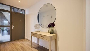 A hallway with a wooden floor, a sliding glass door, a round mirror, and a small table with a vase of flowers. - The Tottenham Hale Crib - Trendy 2bdr Flat With Balcony (London)