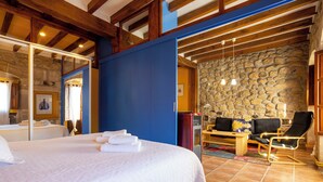 Een hotelkamer met een bed, een zithoek met een bank en stoelen, een stenen muur en een houten plafond.