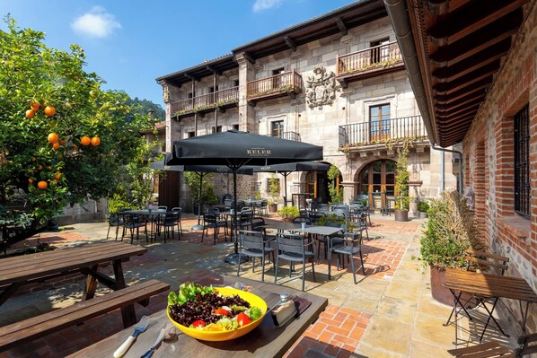 An outdoor patio with tables and chairs, a black umbrella, and a bowl of salad.