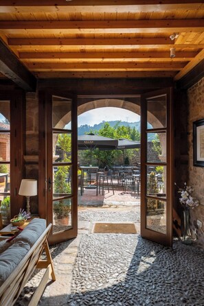 An open doorway leading to an outdoor patio with stone flooring, wooden furniture, and a view of the surrounding landscape. - La casona de las meninas (Cartes)