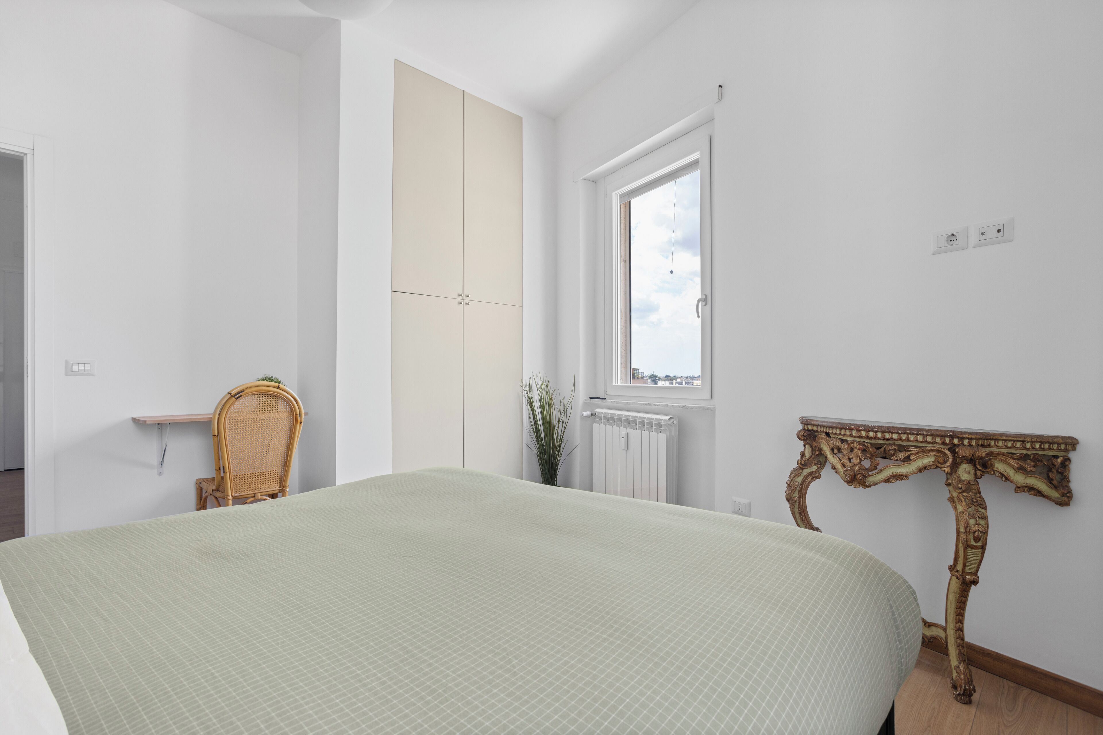 A bedroom with a bed, a chair, a wardrobe, a window, and a table.
