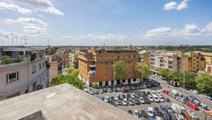 A high-rise building with multiple balconies, a parking lot with various cars, and a clear blue sky with scattered clouds. - Sunny House Gianicolo (roma)