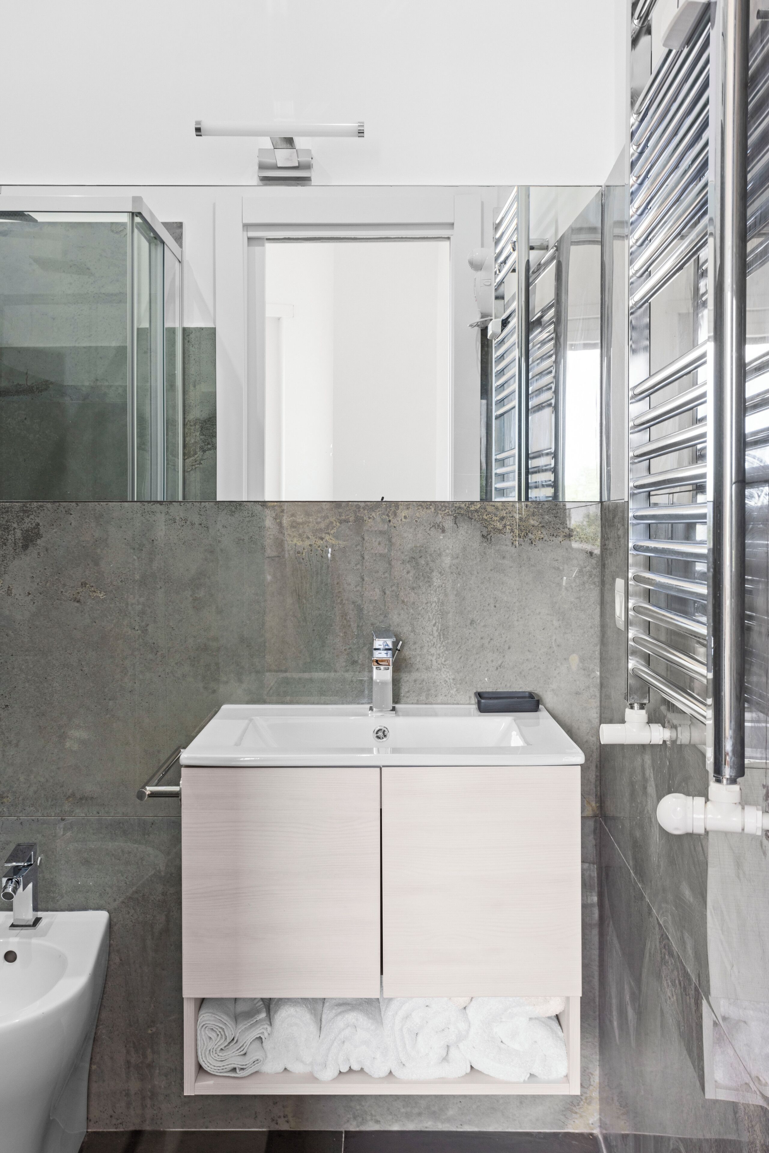 A modern bathroom with a white sink, a mirror above it, and a towel rack to the right.