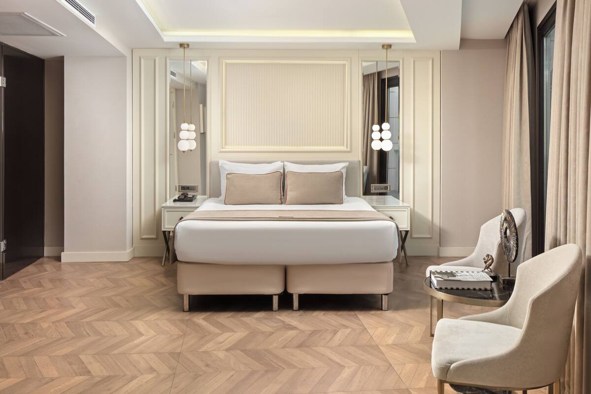 A modern hotel room with a large bed, bedside tables, a chair, and a mirror.