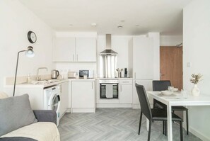 A compact kitchen with a washing machine, oven, and dining area with chairs.