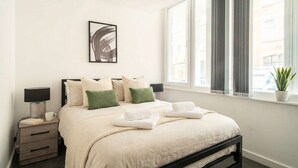 Een hotelkamer met een bed, nachtkastjes, een raam met gordijnen en een ingelijste foto aan de muur.