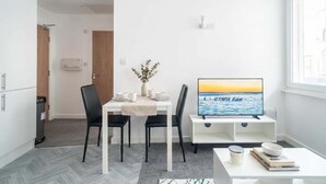 Een moderne, minimalistisch ingerichte kamer met een eettafel, twee stoelen, een televisie en een raam met uitzicht op zee.