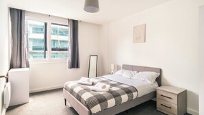 A modern bedroom with a bed, bedside table, and a window with curtains. - Central Preston Lovely 1 Bedroom Apartment (Preston)