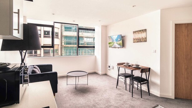 A modern living room with a sofa, a small round table, and a TV mounted on the wall. - Central Preston Lovely 1 Bedroom Apartment (Preston)
