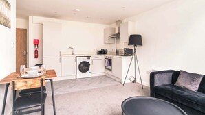 A compact living space with a kitchenette, a dining area, a sofa, and a floor lamp. - Central Preston Lovely 1 Bedroom Apartment (Preston)