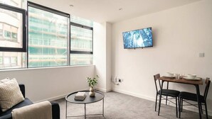 A modern room with a large window, a small round table, a dining table with chairs, and a mounted TV. - Spacious 1 Bed Apartment in the Heart of Preston (Preston)