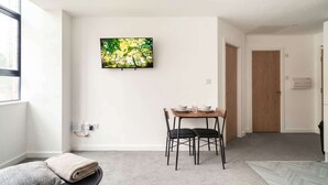 A modern room with a dining table, chairs, a TV mounted on the wall, and a window. - Spacious 1 Bed Apartment in the Heart of Preston (Preston)