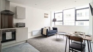 A modern kitchen with a microwave, oven, and cabinets. There is a dining area with a table, chairs, and a lamp. - Spacious 1 Bed Apartment in the Heart of Preston (Preston)