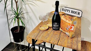 A small table with a bottle of wine, a glass, and a loaf of bread. There is a sign that reads "HAPPY HOUR" and a potted plant beside the table. - Close to Leeds Centre - The Snug Apartment (Leeds)