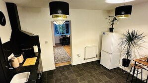 A modern kitchen with dark tiles, a built-in oven, and a dining area with a table and chairs. - Close to Leeds Centre - The Snug Apartment (Leeds)