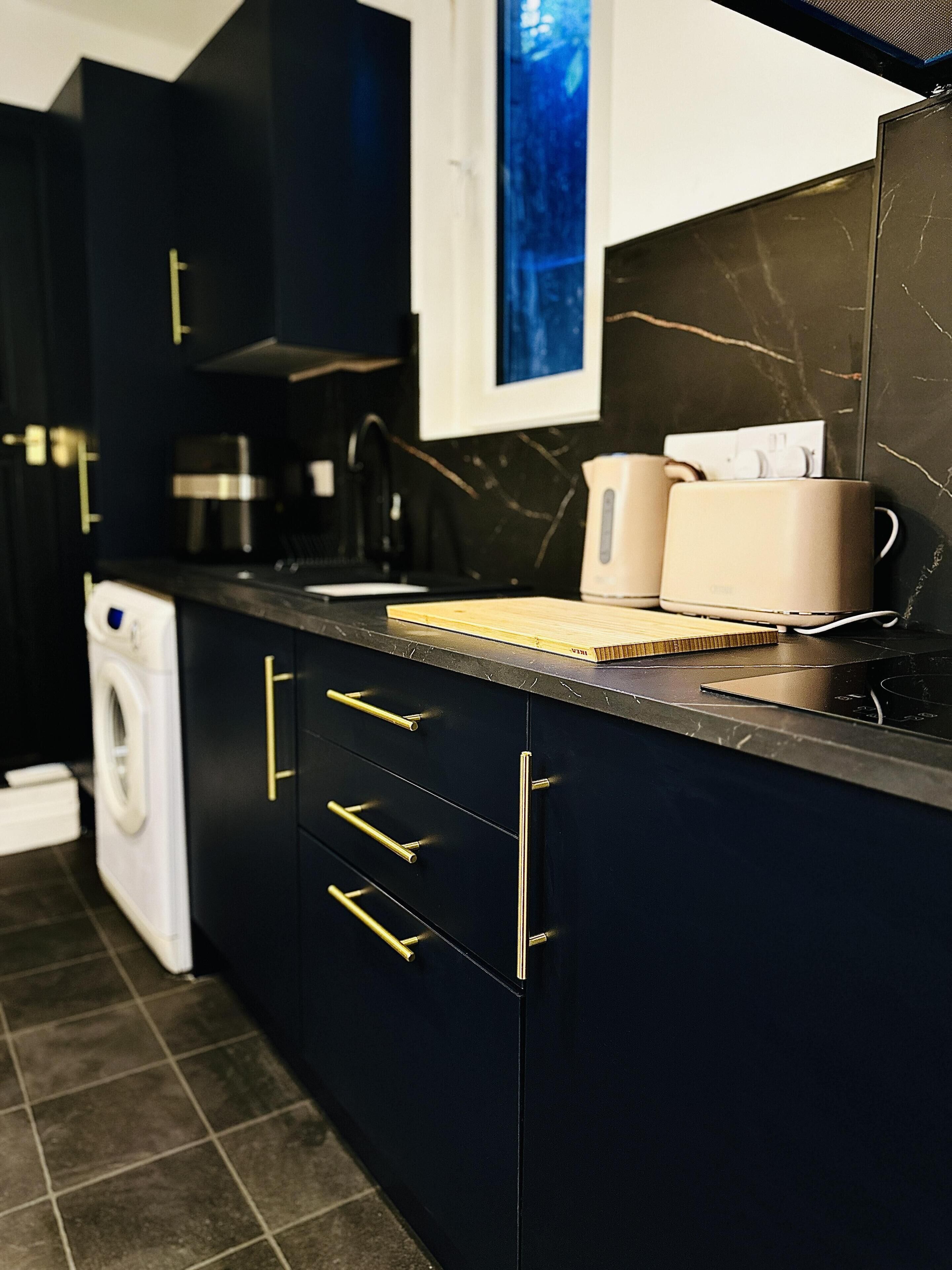 A modern kitchen with dark cabinetry, a stainless steel range hood, and a coffee machine.