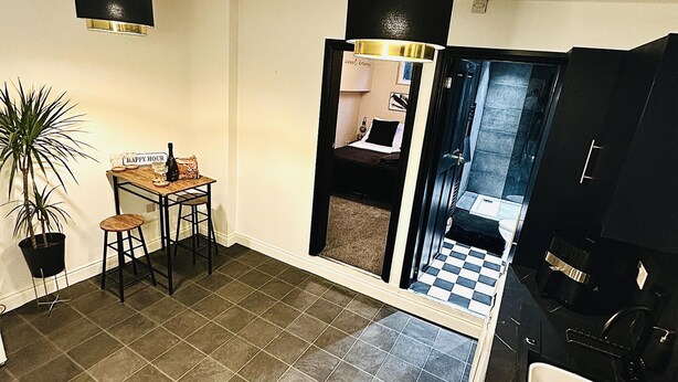 A compact living space with a kitchenette, a dining area with a small table and chairs, a potted plant, and a checkered floor. - Close to Leeds Centre - The Snug Apartment (Leeds)