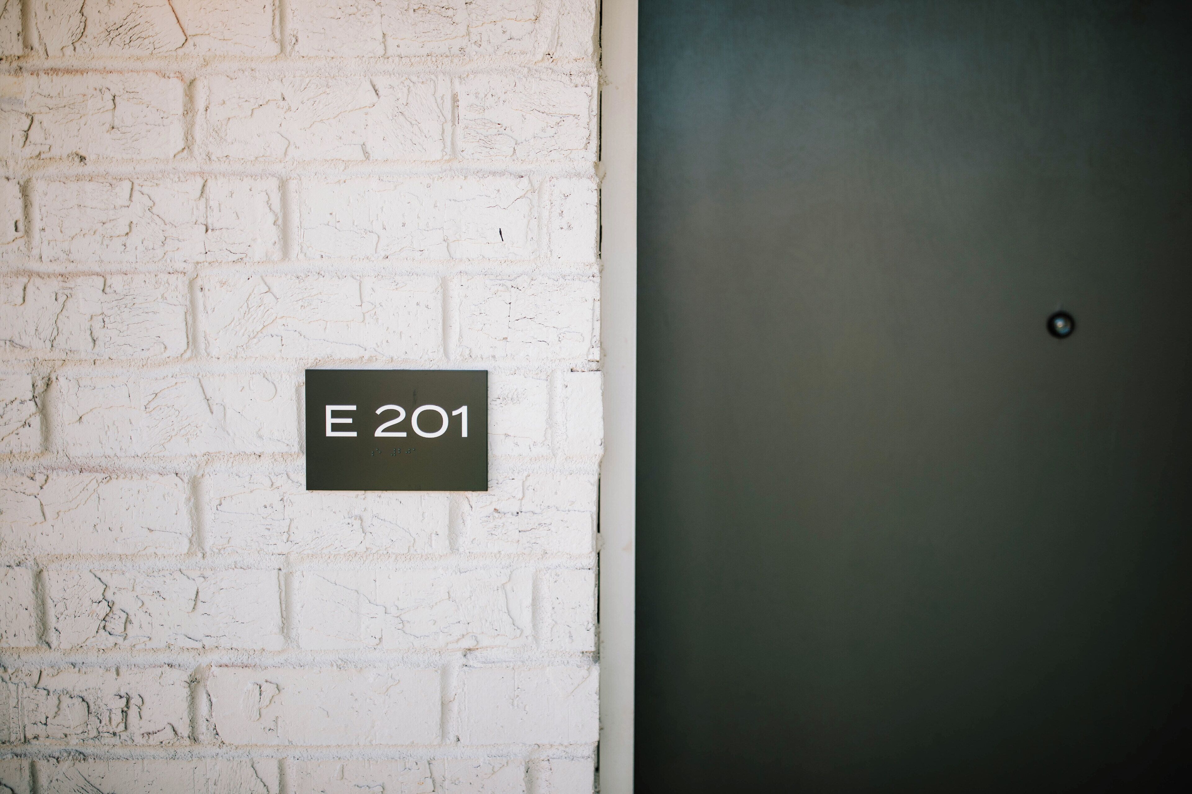 A white brick wall with a sign reading "E 201".