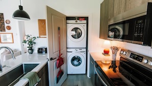 A compact kitchen with a washing machine, microwave, and stove. - Cozy 1BR Home by MHM Luxury Properties (Athens)