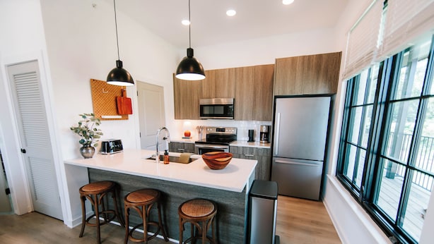 A modern kitchen with a central island, bar stools, stainless steel appliances, and large windows. - Cozy 1BR Home by MHM Luxury Properties (Athens)