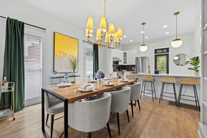 Una cocina moderna con armarios blancos, un refrigerador de acero inoxidable y un comedor con mesa de madera y sillas grises.