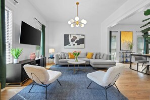 Una sala de estar moderna con un sofá gris, dos sillones blancos, una mesa redonda de centro y un cuadro grande en la pared.