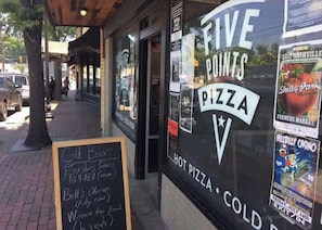 Une devanture de magasin avec une enseigne indiquant « Five Points Pizza » et un tableau noir affichant le menu, avec des articles tels que « bière fraîche » et « Foulers' Door ».
