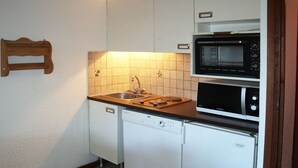 A compact kitchen with white cabinets, a microwave, a dishwasher, and a wooden countertop.