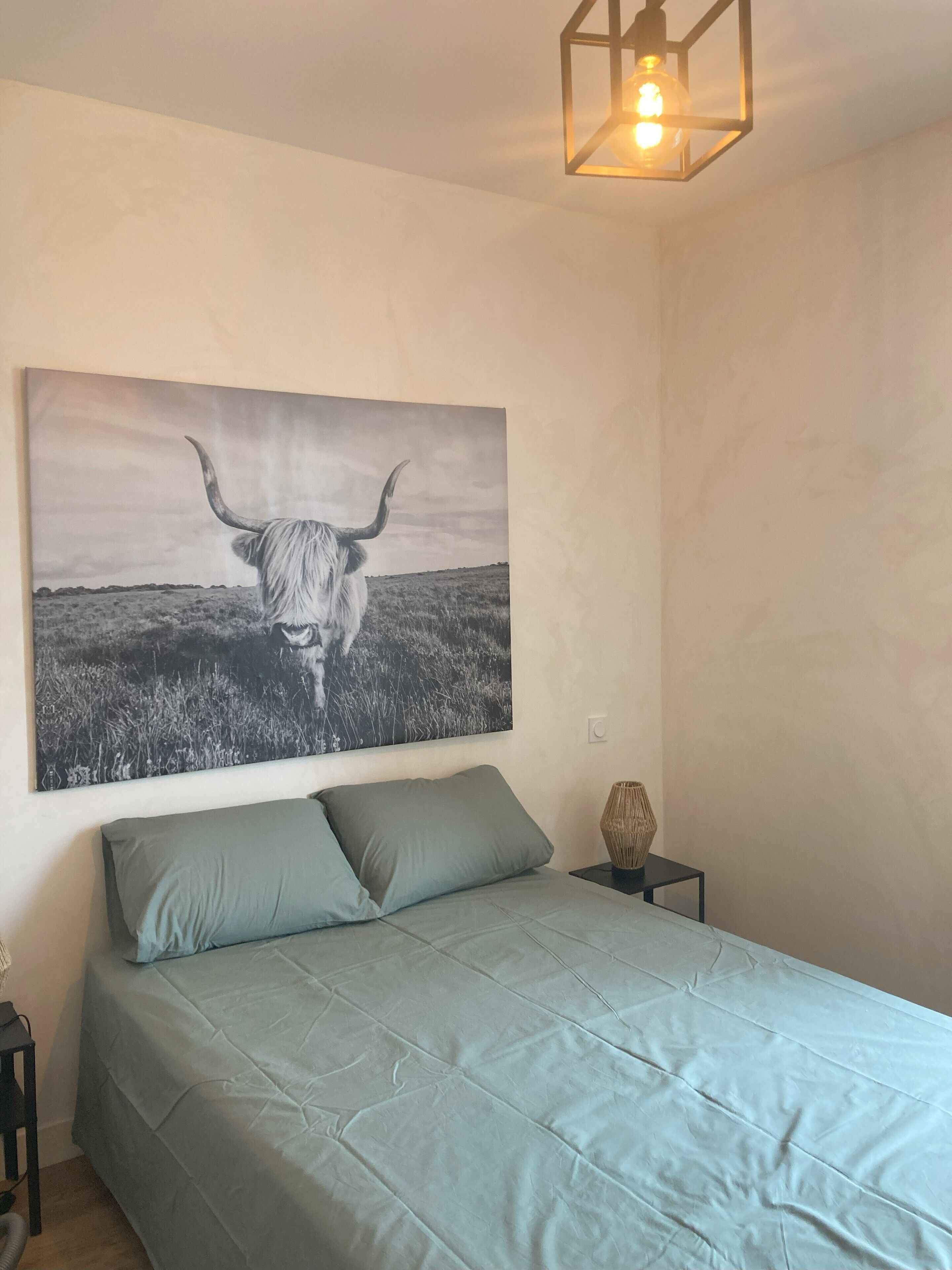 A bedroom with a bed, pillows, a nightstand, a lamp, and a wall-mounted picture of a bull.