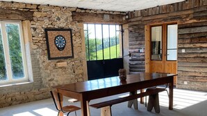 A spacious room with a large wooden table, a stone wall, and a window with a view of greenery. - Gîte au Cœur du Beaujolais, Dans un Domaine Viticole (buuly)