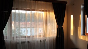 A bedroom with a bed, a radiator, a window with curtains, and a ceiling fan.