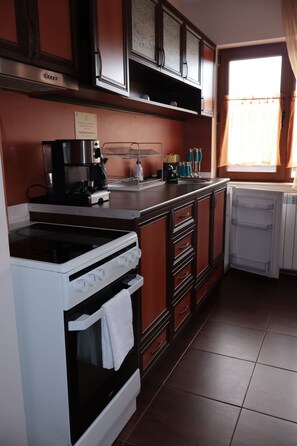 Una cocina con estufa, horno, refrigerador y una ventana con cortinas.