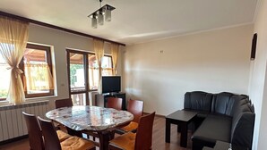 A modern living room with a round dining table, leather sofa, and a flat-screen TV.