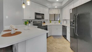 Eine moderne Küche mit weißen Schränken, einem Edelstahl-Kühlschrank, einer Mikrowelle und einer großen Kochinsel mit Spüle.