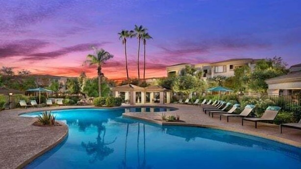 Ein Poolbereich eines Resorts mit Liegestühlen, Palmen und einem Sonnenuntergangshimmel.