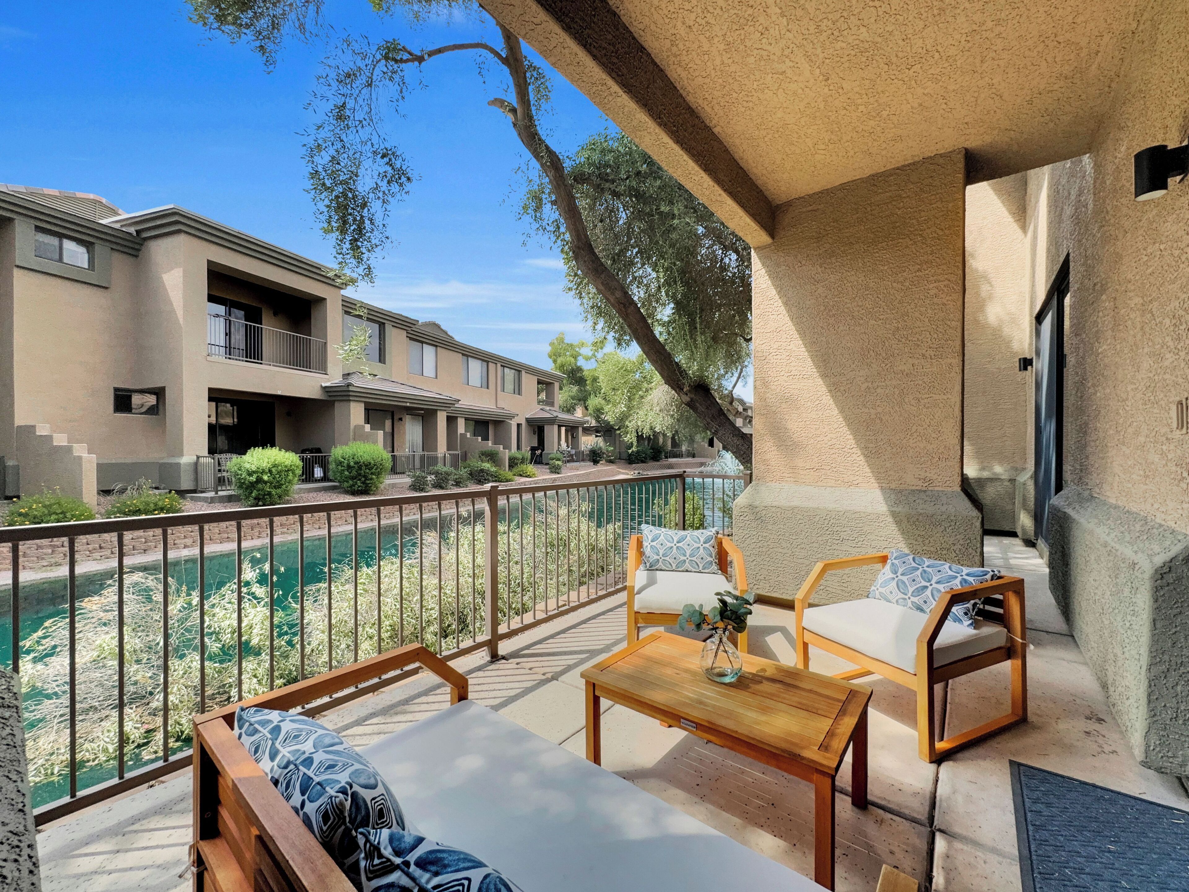 A balcony with wooden furniture, a small table, and a view of a pool and buildings.