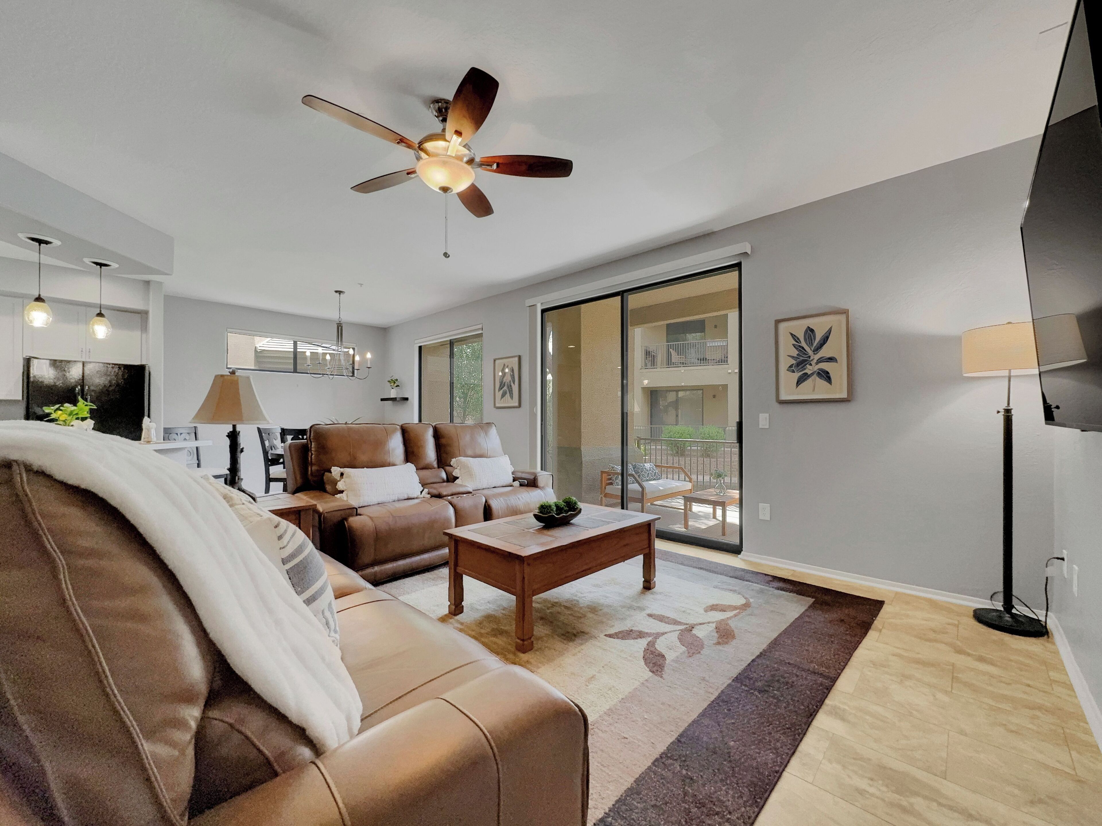 A modern living room with a ceiling fan, leather sofas, a coffee table, and a view of a balcony.