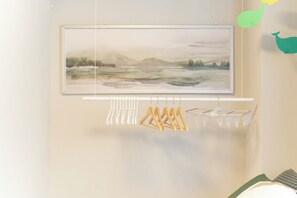 A room with a framed landscape painting, a drying rack with clothes, and a bed with a green cover. - Fiore Kinshicho by Tranova (Tokyo)