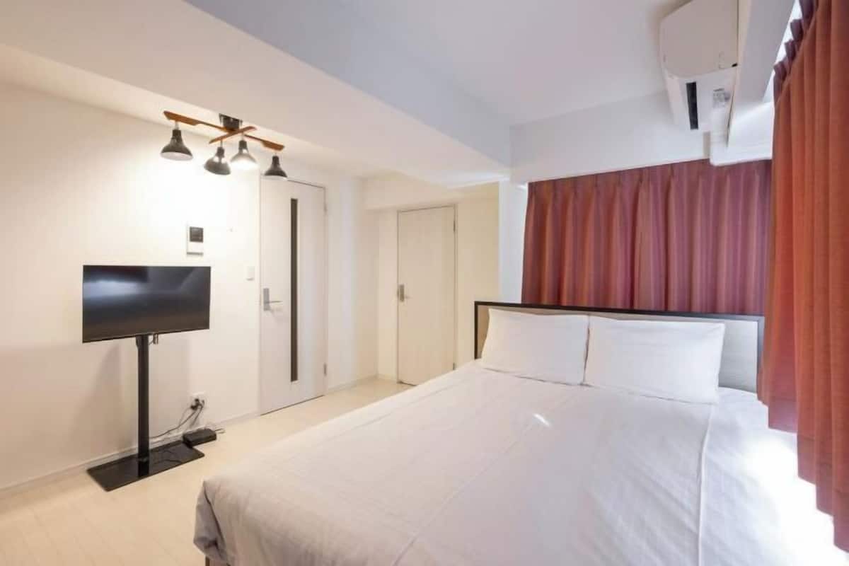 A hotel room with a bed, a flat-screen TV, a ceiling fan, and an air conditioning unit.