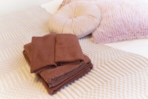 A neatly folded brown towel on a textured beige bedspread with a round beige pillow and a fluffy pink pillow. - Fiore Kinshicho by Tranova (Tokyo)