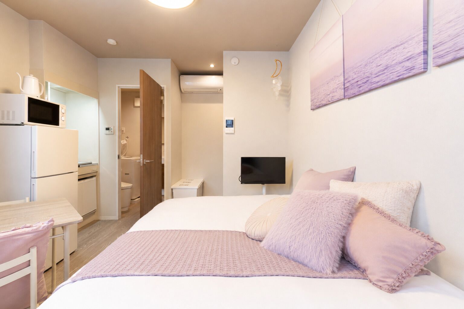 A bedroom with a bed, a television, a desk with a computer, and a kitchenette.