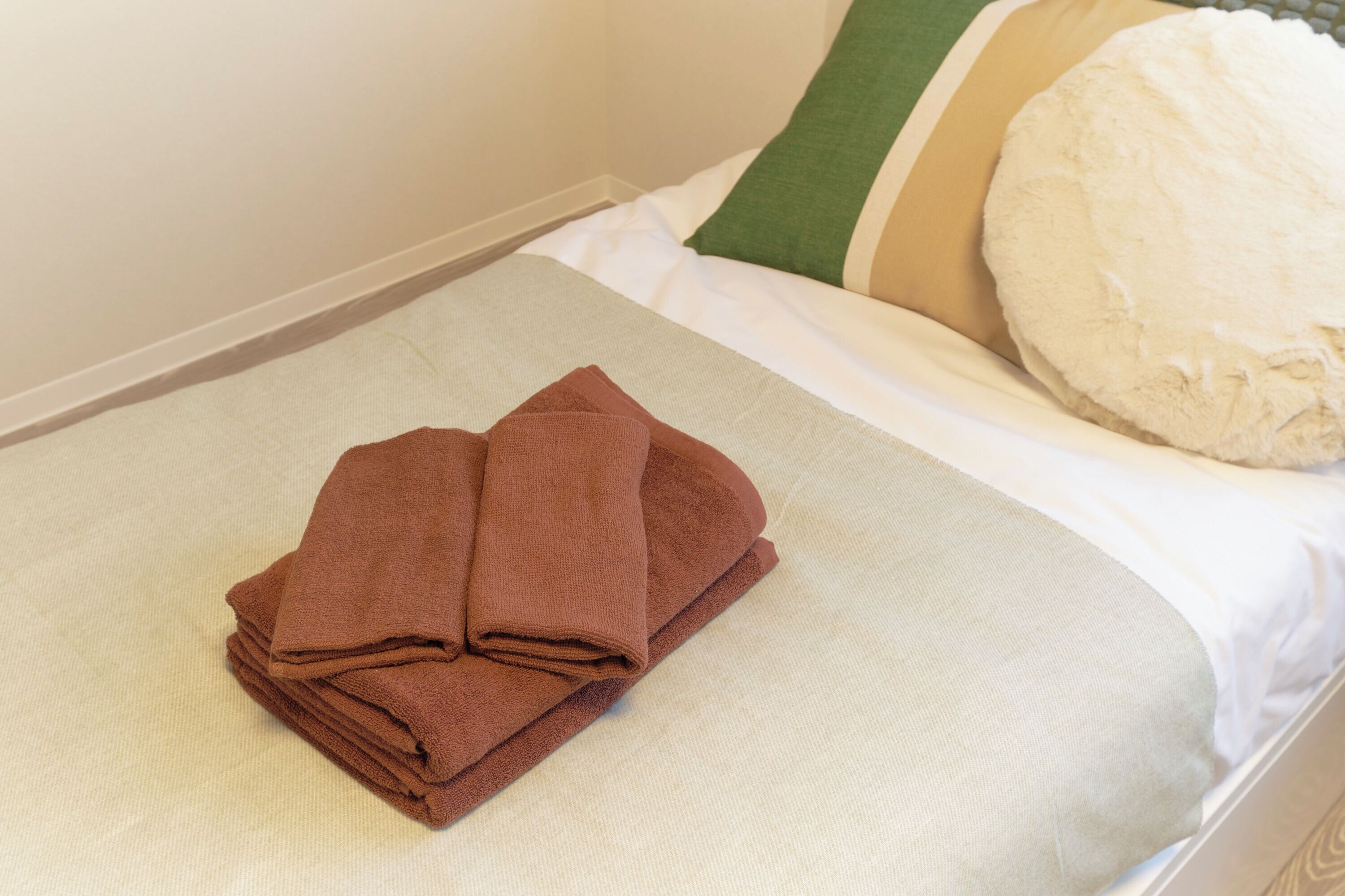 A neatly made bed with a folded brown towel and a pillow with a striped pillowcase.
